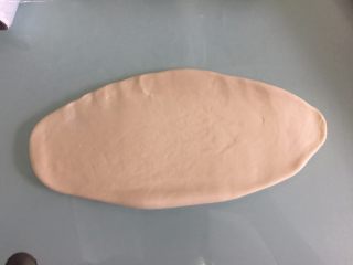 4、德国碱水面包普雷结,取1个面团擀成椭圆形,卷起来捏紧收口