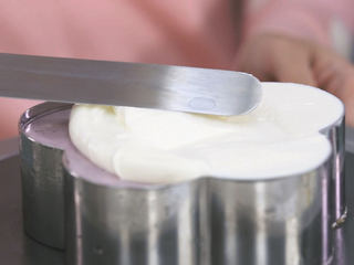 15、蓝莓益力多慕斯,因为慕斯是没有满模的,我们把打发好的淡奶油抹进去慕斯圈的顶部,用抹刀抹平,然后把慕斯脱模,那慕斯就做好喽