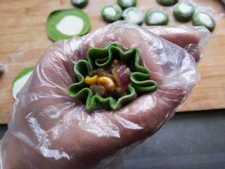 15、翡翠烧麦,取一个面皮放上炒好的糯米肉馅，用左手虎口把烧麦的边缘收拢，在烧麦的腰部用力捏一下，一边旋转收拢一边整理边缘。包好后把边缘往外拉一拉，造型就出来了。