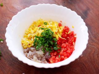 4、番茄虾仁鸡蛋水晶蒸饺,把炒熟的鸡蛋放入一个大一点的容器里,加入切碎的番茄和虾仁,再放入切碎的小葱。