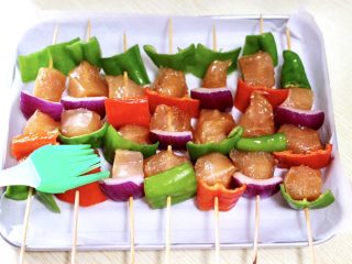 9、时蔬孜然烤鸡肉串,把腌制好的鸡胸肉，用竹签串起来，把洋葱和青红椒也串到鸡胸肉中，烤盘里铺上油纸，把串好的鸡胸肉串，放到烤盘里，用刷子蘸花生油涂抹一遍。
