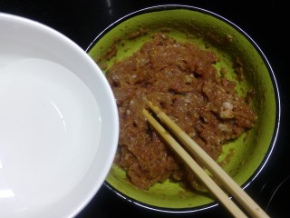6、豆角焖肉饼,分次加入清水顺着一个方向搅打上劲。
