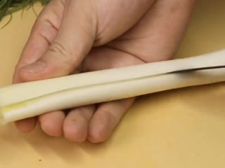 3、葱油鲈鱼,大葱段先划一刀,再给它延展摊开,然后和葱一样对折卷起来