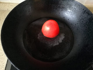 3、酸甜年糕,取一锅，放少量水，烧开，将西红柿顶部切个十字，放入开水里滚上一圈后捞出，将皮撕掉。