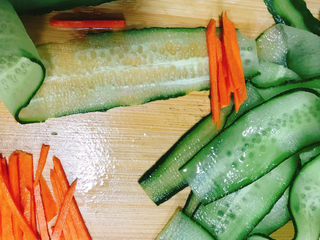 5、凉拌黄瓜卷,取几条胡萝卜丝放在青瓜薄片上。