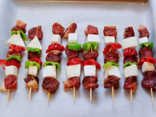 11、时蔬美味牛肉串,取一根牙签，一块肉，一款杏鲍菇，一块彩椒，这样串起来，依次串完所有的牛肉，烤盘垫上油纸，将串好的牛肉串放入烤盘中。