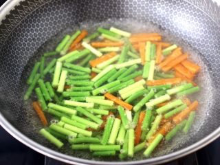 6、蚝香蒜薹鱿鱼小炒,锅中倒入适量清水烧开,倒入少许盐和几滴食用油,先吧胡萝卜进行焯水半分钟,再放入蒜头进行焯水,看见蒜薹和胡萝卜断生变色即可捞出过冷水备用。