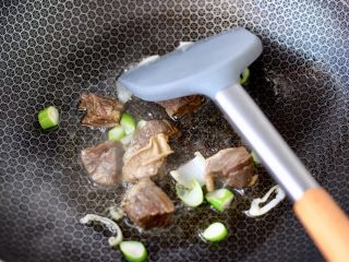 3、番茄牛腩面,锅烧热后倒入花生油烧热,大火先爆香葱碎,再倒入牛腩块快速翻炒片刻。