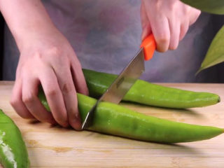 4、往青椒里塞入半斤金针菇，这味道绝了！,接着我们来处理尖椒，用刀子将尖椒对半切开。