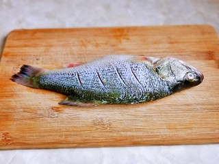 3、红烧鱼,放在砧板上，鱼身两面各划四刀。