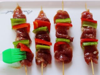 14、超爽的麻辣孜然烤肉串,这个时候用硅胶刷子蘸少许食用油刷在肉串和青红椒身上。
