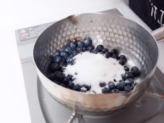 2、梦幻蓝莓冰饮,将蓝莓倒入平底锅里，加白砂糖、加水、开火熬煮