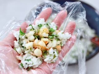 14、香椿红虾饭团,保鲜膜底下铺一层搅拌好的米饭,中间放入适量炒好的馅料。