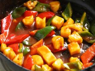 8、菠萝咕噜豆腐,锅内倒入适量油加热,倒入调味汁略炒一下,放入青红椒片和沥干盐水的菠萝块,翻炒片刻,使物料均匀裹上调味汁。