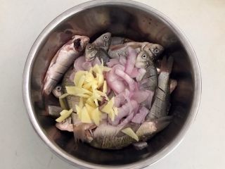 7、干炸鲫鱼,把圆葱片和姜片放入鱼盆里面