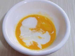 4、10分钟轻松搞定快手早餐～酸奶松饼,加入酸奶，10g细砂糖，玉米油，用手动打蛋器打至均匀！完全融合！