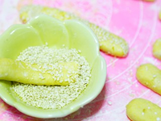 4、香甜软糯的红薯芝麻条,准备一碗清水和一碗芝麻，搓好的圆条先裹上一层水，然后再裹上一层芝麻，然后放在手上搓一搓，让芝麻粘的更加牢固，芝麻条的形状就出来啦。