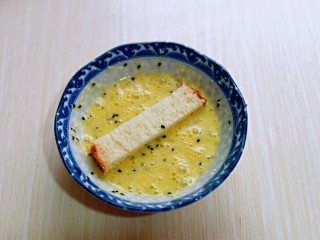 7、简单快手小零食~黑芝麻椰香吐司条,取一条吐司条,放入蛋液中,均匀裹上蛋液。