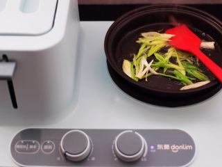 4、土豆丝红椒煎春卷,东菱早餐机的煎锅里，倒入花生油烧热后，先放入切好的一半蒜苗爆出香味。