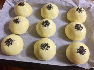 13、红豆沙餐包,发至两倍大,手指轻压表面不会马上回弹又显得有张力时,就说明发酵好了。二次发酵结束后,表面刷蛋液,擀面杖蘸水后,沾上黑芝麻,然后将黑芝麻印在面包表面中间。