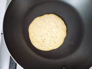 15、【宝宝辅食】无油香蕉牛奶鸡蛋松饼,煎到面饼上面都冒出了小气泡的时候，准备翻边。如果面饼的小气泡都集中在一个地方，别的地方没有小气泡的话，那就是受热不均匀，记得把锅子拿起来移动一下。