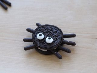 13、万圣节蜘蛛杯子蛋糕,盖上另一片饼干，轻轻压一下，再将眼睛糖豆蘸少许淡奶油，粘到饼干上面，蜘蛛造型就完成了