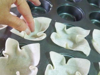 3、缤纷花杯~年菜,将馄饨皮塞进马芬模中，抓出花瓣形状。