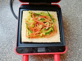 7、全麦蔬菜三明治,预热好的三明治早餐机下盘放上一片全麦吐司，放上炒好的蔬菜。
