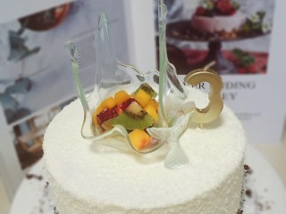 17、艾素糖造型水果蛋糕,抹面不用非常平整，因为蛋糕底部粘了一层奥利奥碎，其余部分粘了一层椰蓉，看起来有颗粒感，更像是白色的沙滩。把艾素糖排在大面上，再放些水果丁，就完成了。