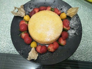 10、水果伴蛋糕,将蛋糕放入盘中，周边围上草莓，再放几颗菇娘果，洒上糖粉，再放几片薄荷叶做装饰即可。