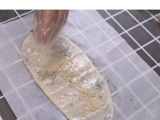 14、梅干菜烧饼,在做好的烧饼上抹上一层油,再均匀来一点白芝麻,是不是已经烧饼的模样出来了。提醒:一定要放在油纸上擀哟