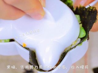 15、杂蔬鳕鱼猫饭团—宝宝从此爱上吃蔬菜,再来做一只黑猫，用剪刀在海苔上剪出猫的轮廓，将海苔放入模具，接着放入米饭，压出猫的形状后将黑猫倒扣在盘子里。