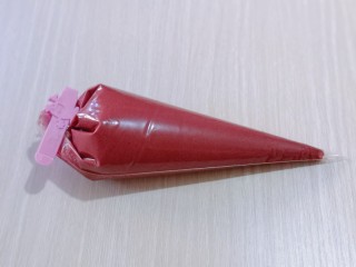 9、红丝绒玛德琳蛋糕,装入裱花袋中，用夹子将其夹紧！放冰箱冷藏室1小时。模具中刷上一层薄薄的玉米油，将蛋糕糊从冰箱取出室温放置2分钟！