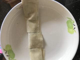 2、云吞皮葱油饼,将5块云吞皮铺平，然后抹油放葱，对折然后卷起来，压扁