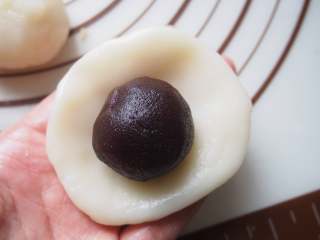 15、豆沙藜麦冰皮月饼,将冰皮放在手心压扁,放入豆沙藜麦馅包起来。