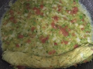 8、宝宝辅食之番茄芝士厚蛋烧,将卷起的蛋饼放在平底锅的一边，将剩余的蛋液倒入锅里。