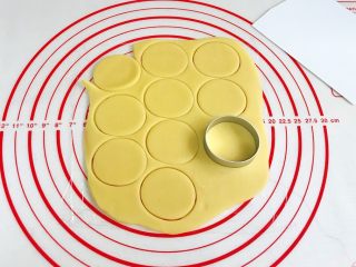 9、小猪曲奇,在硅胶垫上铺一层保鲜膜,把原色面团擀成约3毫米厚度的薄片,用椭圆形的饼干模具压出形状,然后借助刮刀把饼干面片移到烤盘上。