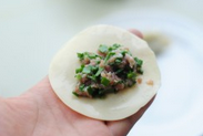 7、鲜肉韭菜锅贴,取一张水饺皮,铺上韭菜肉馅。