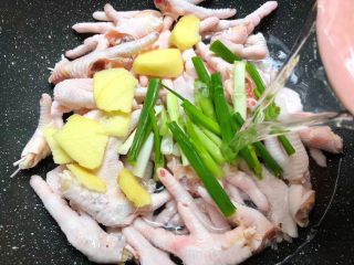 4、酸辣泡爪,把切好的鸡爪放入锅里，加入葱段和20克姜片，倒入适量水，大火把水烧开焯出血末。