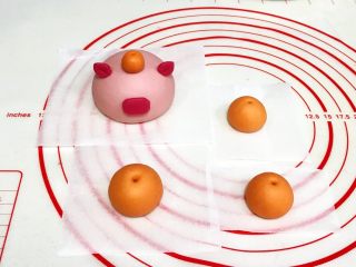 11、吉祥如意小猪馒头,把橘色的面团分出1个3克小剂子搓圆,粘在小猪的脑袋上,其余的面团随意分成3份滚圆,用尖的筷子或竹签在圆面团上扎个孔。
