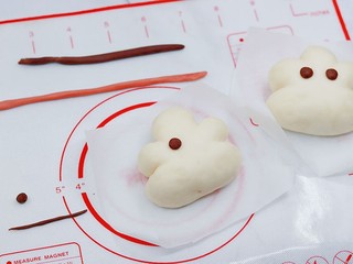 7、云朵馒头,在云朵脸部涂上少量牛奶。取约绿豆大小的棕色面团，搓成圆粒，做成不同心情的眼睛。眼睛放在云朵面团上，稍微压平。