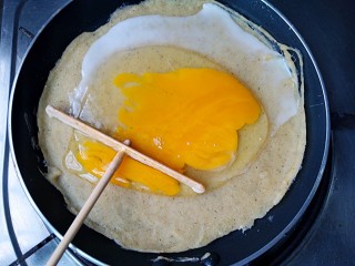 6、杂粮煎饼,待煎饼周围开始翘起时，在煎饼上打上个鸡蛋，用推子将鸡蛋敲散，均匀铺满煎饼上。
