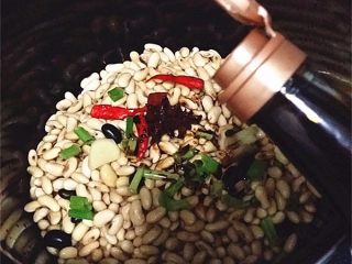 3、黄豆煲鸭翅,黄豆、葱姜、八角、桂皮、香叶和干辣椒放入电饭煲中再倒入适量老抽