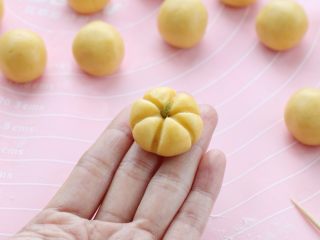 8、南瓜饼干,用牙签在小圆球上压出南瓜的纹路，再把葡萄干切成细条插在上面当做南瓜梗，这样一个南瓜的造型就完成了