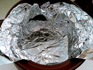 3、坤博砂锅烤紫薯,裁两张比锅体大的锡纸备用。锡纸放入锅内，一圈用手按压贴牢砂锅内壁，顶部包住砂锅边沿。