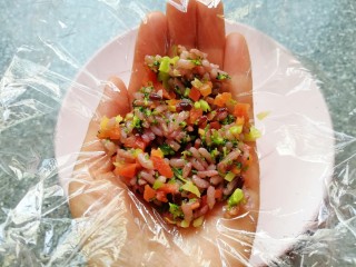 10、杂粮蔬菜饭团,手掌心里放上一张保鲜膜，舀入拌好的杂粮蔬菜饭，提起保鲜膜的四个角，用手捏好饭团。
