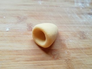 10、玉米粉窝窝头,将圆锥形的面团放在左手手心里,用右手的大拇指放在圆锥形底部的中间位置,转圈旋出窝头的窝。