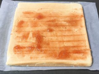 15、草莓酱蛋糕卷,冷却一下，蛋糕移至烤盘纸上，表面铺上草莓果酱，至于放多少可以自由发挥，我的观点是簿簿的一层。