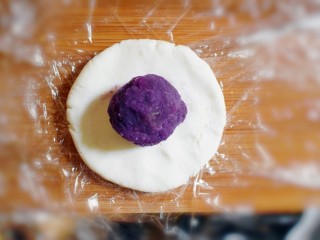 12、紫薯山药糯米饼（微笑饼）,取一个剂子，用手压成饼状，并取一个紫薯泥团子，放在饼上。