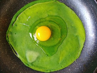 10、菠菜煎饼果子,在上面放一个生鸡蛋。戳碎，平摊到面饼上。